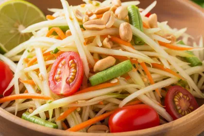 Colorful bowl of authentic Thai green papaya salad with shredded vegetables, tomatoes, and peanuts.